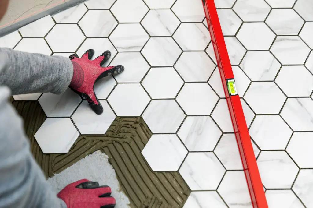 Worker installing marble texture hexagon tiles on the bathroom floor