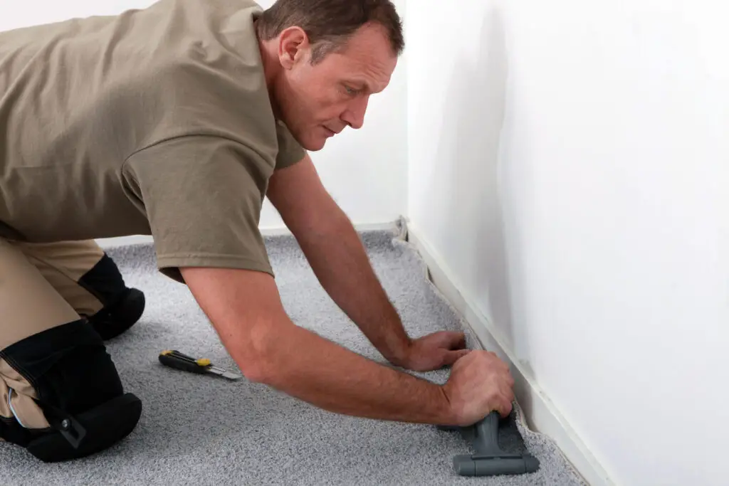 Installer fitting carpet along baseboard in residential room